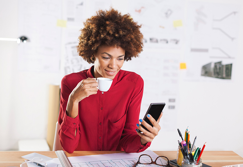 young woman drinking at desk using mobile phone young woman drinking at desk using mobile phone